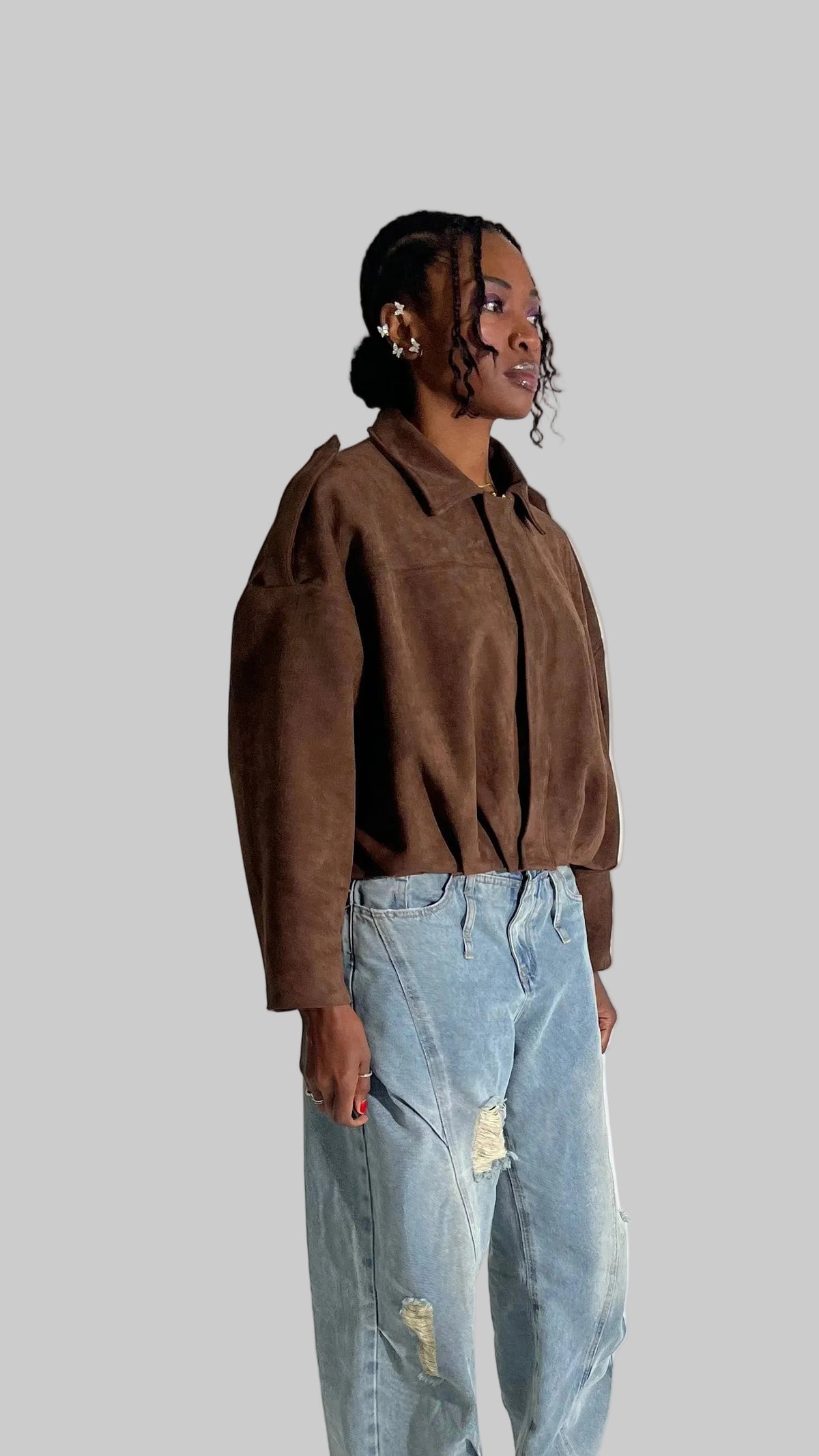 Person wearing a brown jacket and light blue jeans against a white background