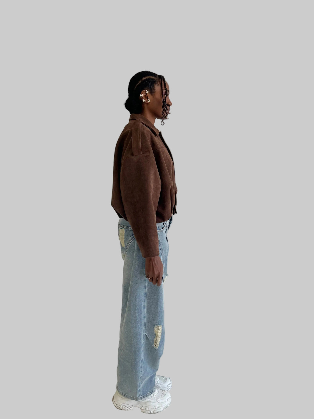 Person wearing a brown jacket and light blue jeans standing against a plain background