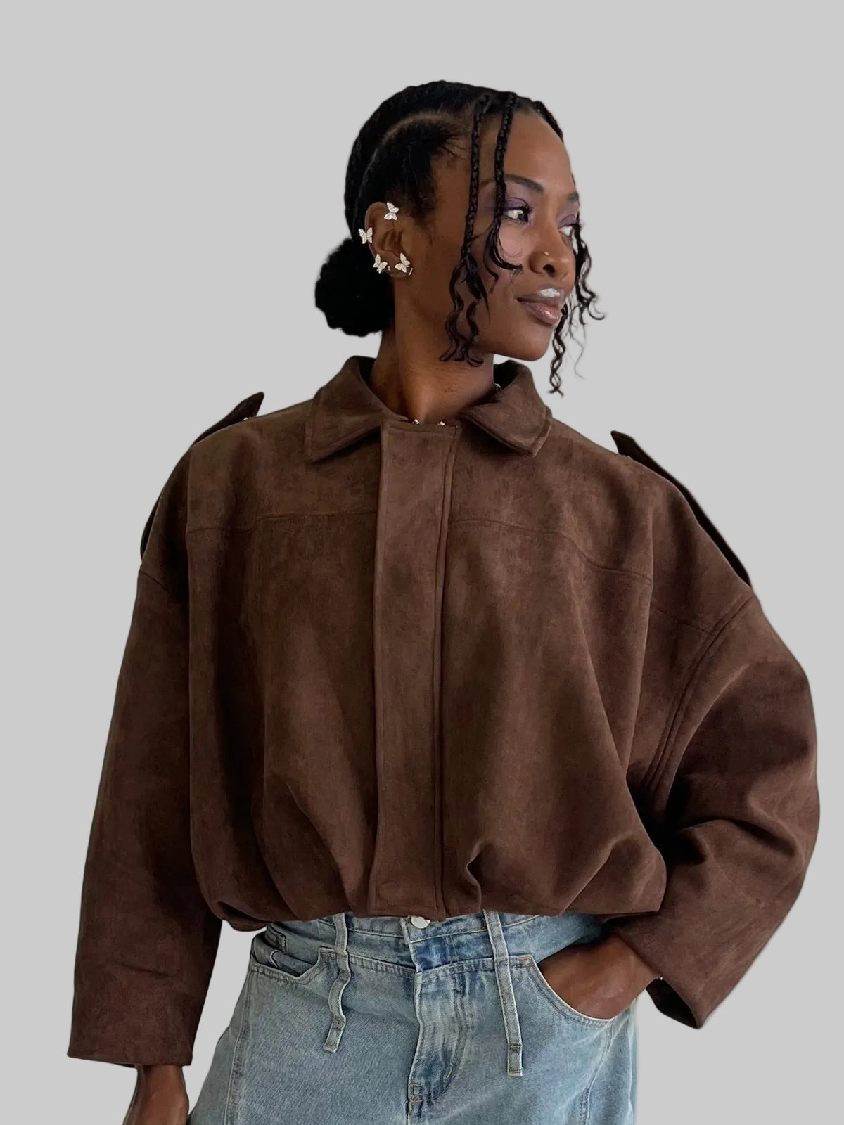 Woman wearing a brown suede jacket and blue jeans against a plain background
