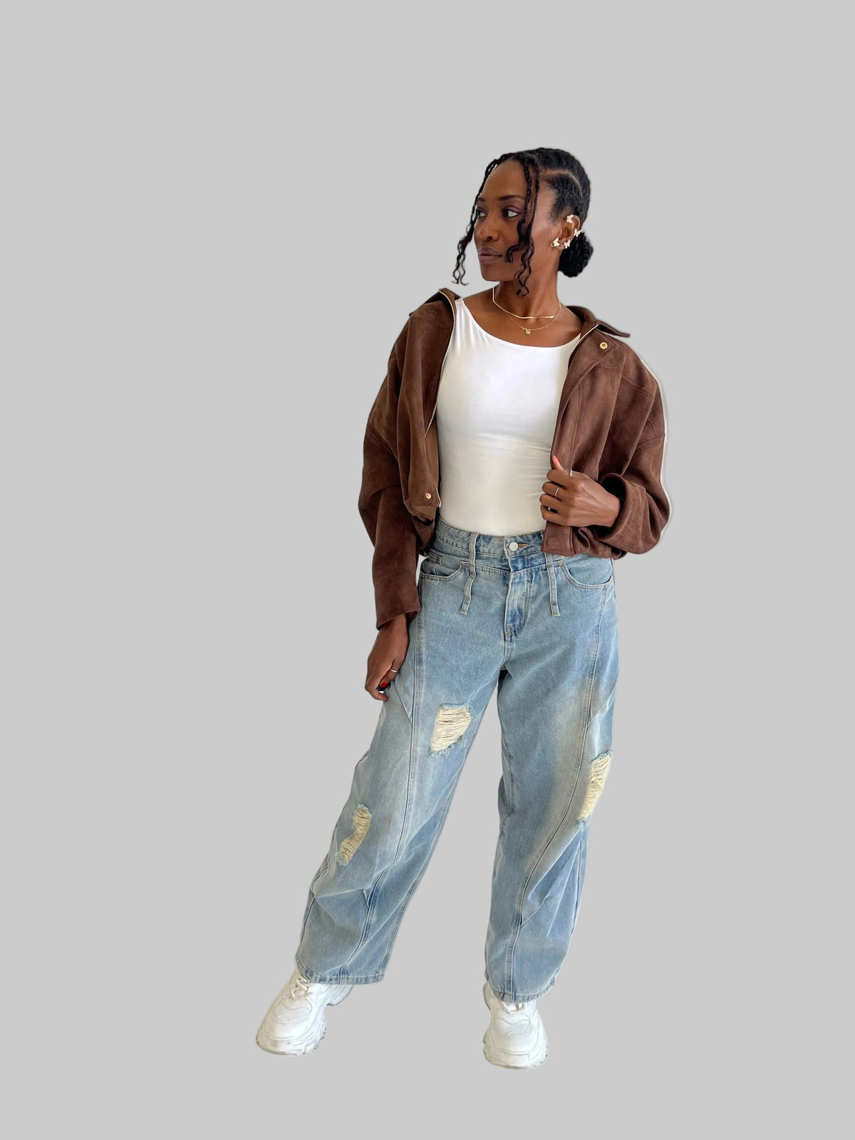 Person wearing a brown jacket, white top, and light blue jeans on a plain background