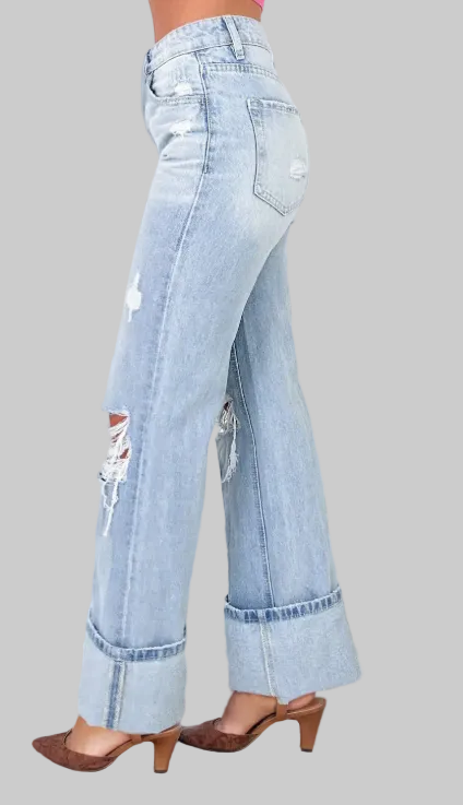 Light blue jeans with distressed details worn by a person, standing on a wooden surface with a blurred background.