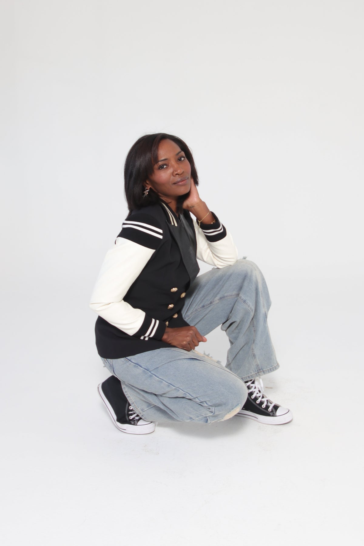Person wearing a black and white varsity jacket with light blue jeans on a white background