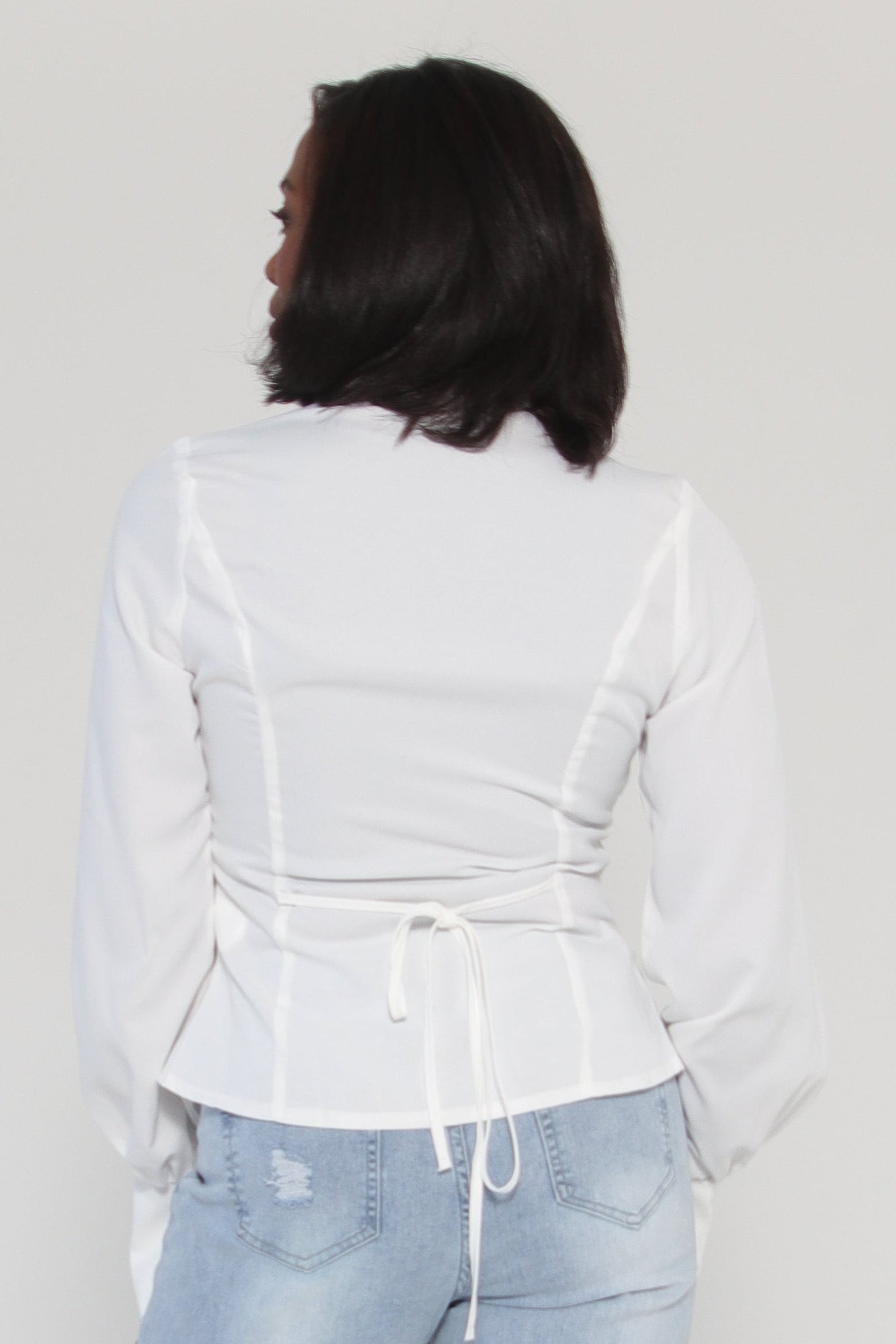 Person wearing light blue jeans and a white jacket on a plain background