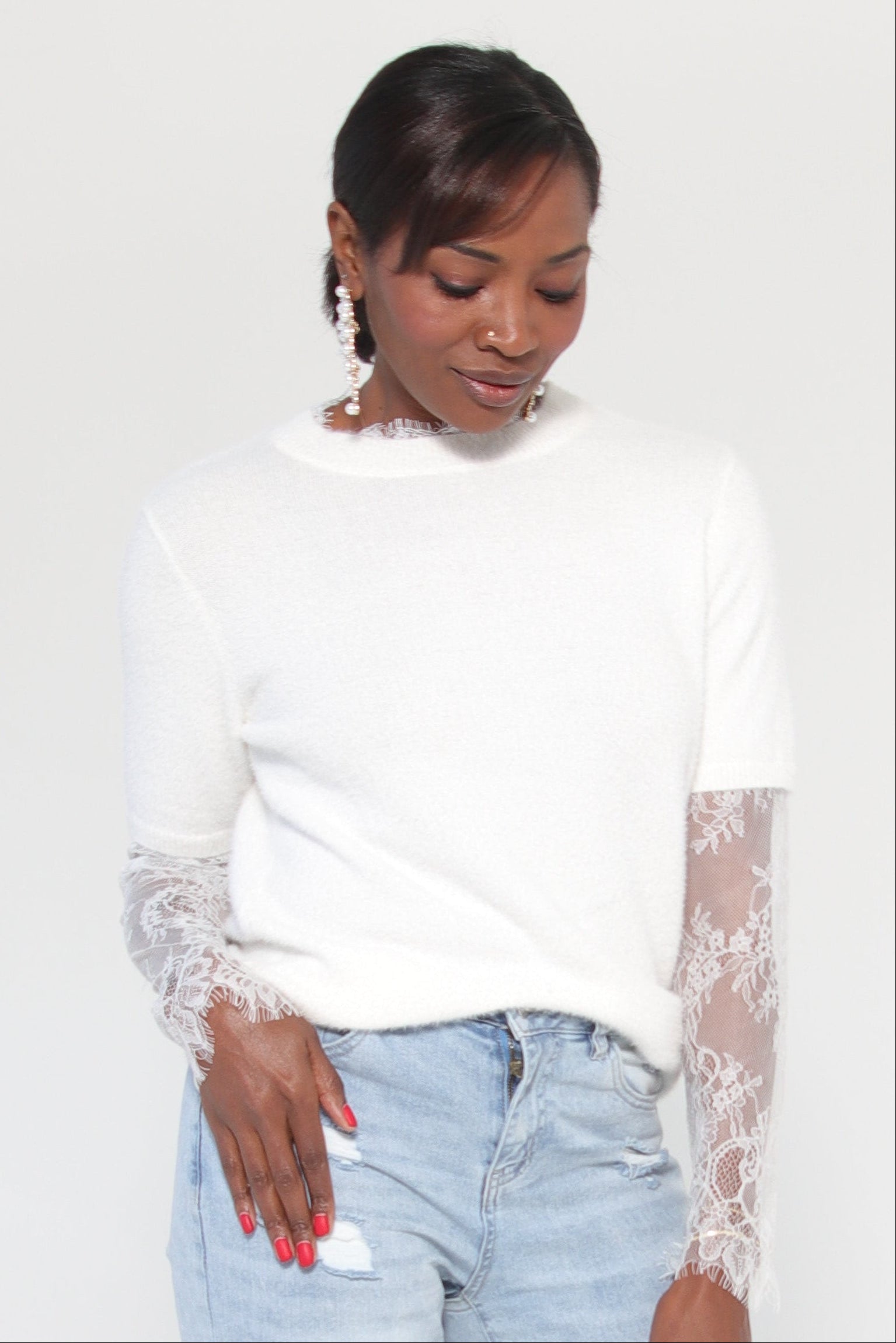 Woman wearing a white sweater with lace sleeves against a white background