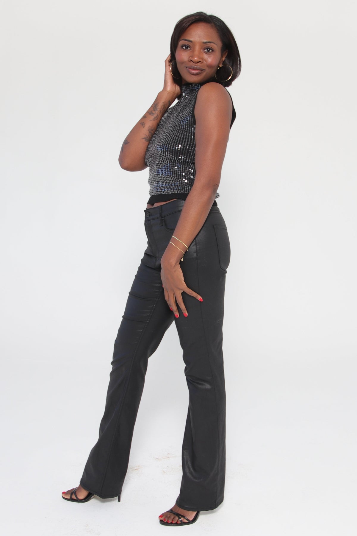 Person wearing a black sleeveless sequin top with coated black pants on a white background
